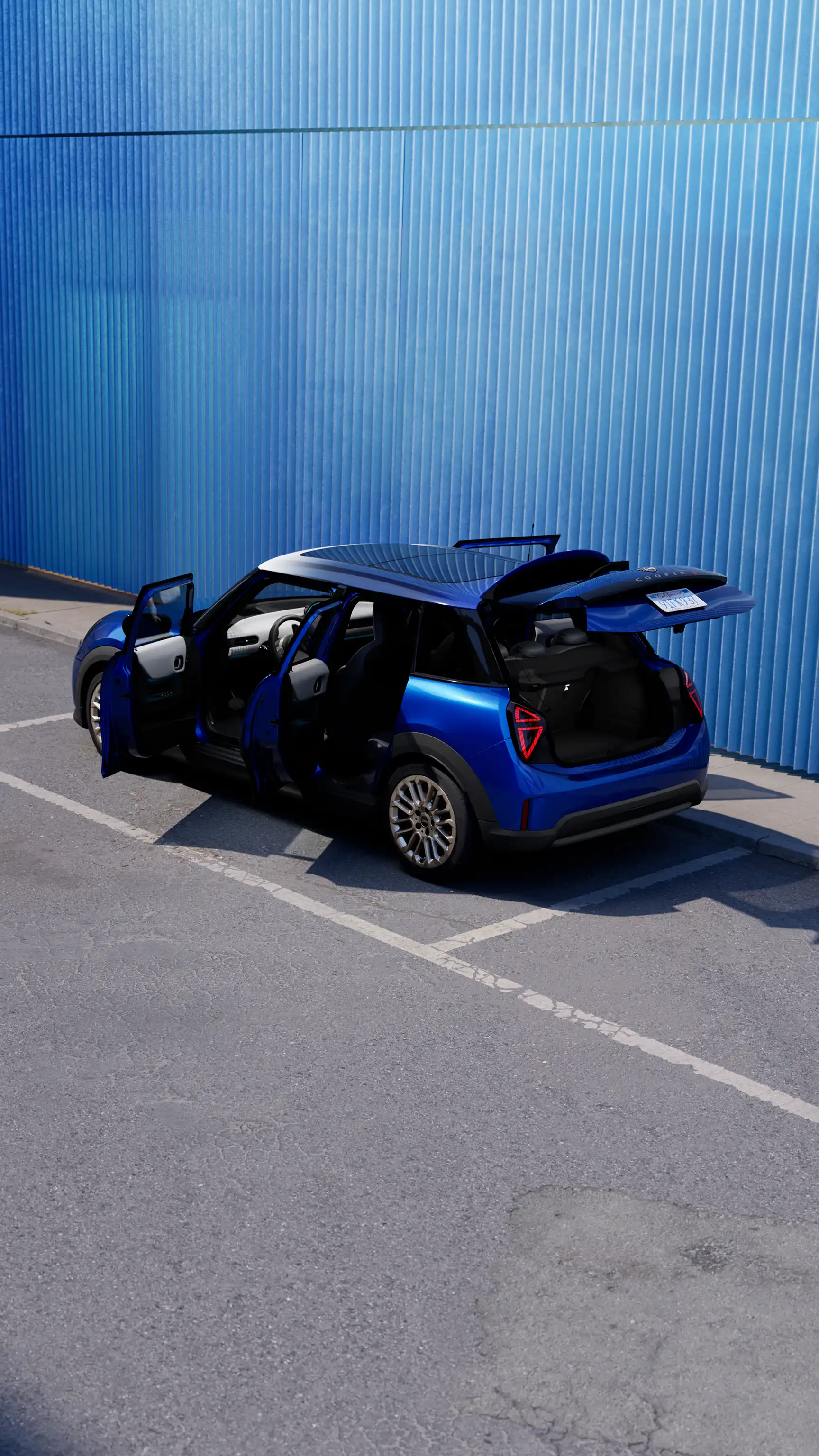 MINI Cooper 5 Doorin Blazing Blue Metallic parked with all doors and tailgate open beside a blue industrial wall.