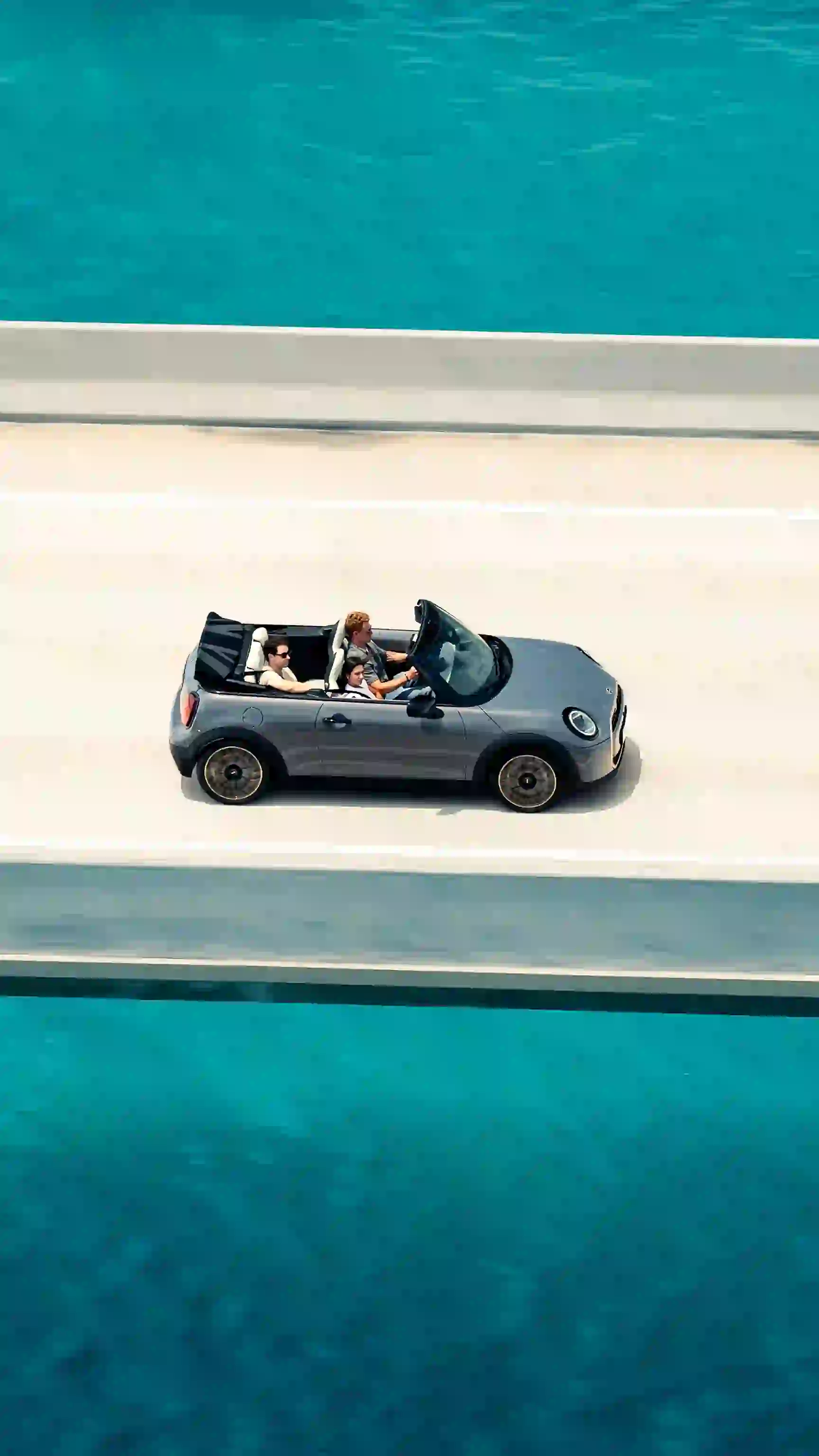 MINI Convertible driving along a coastal road with passengers seated inside.