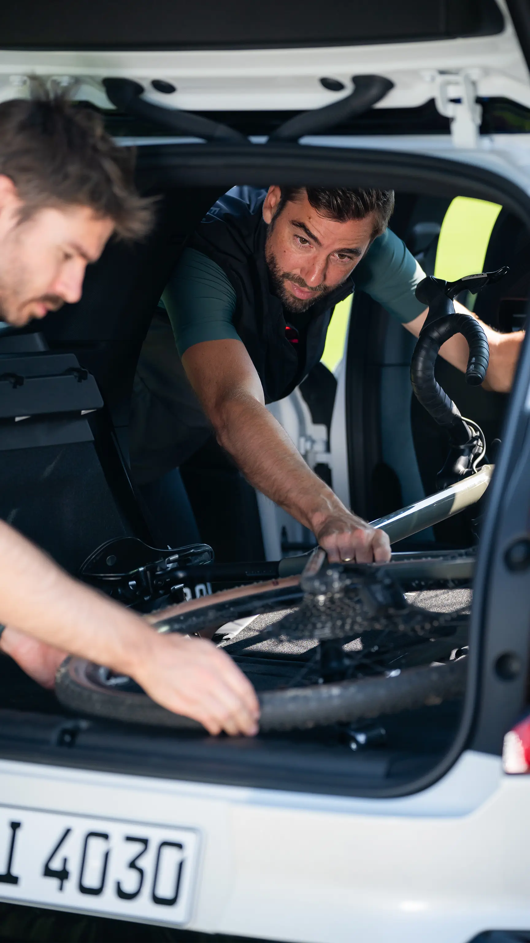 Two people loading a bicycle into the back of a MINI vehicle through the open boot.