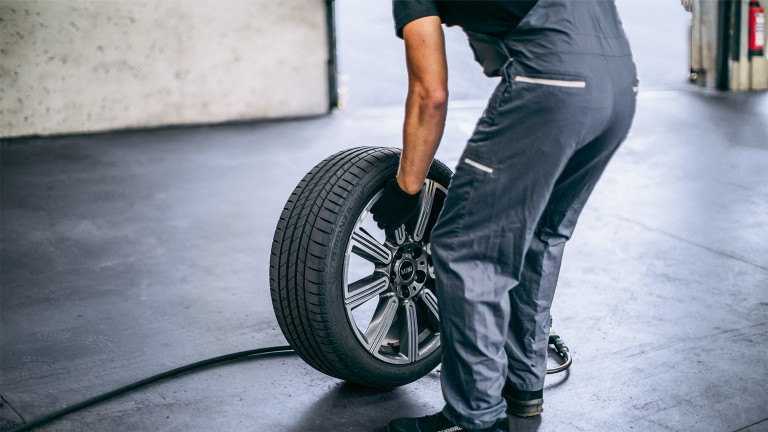 MINI Service center employee in a grey robe changing a wheel rear view.